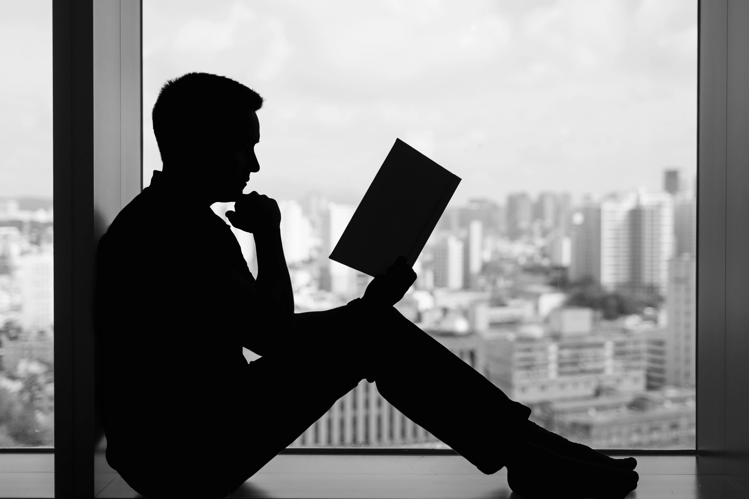 Executive reading a book by a window with city skyline